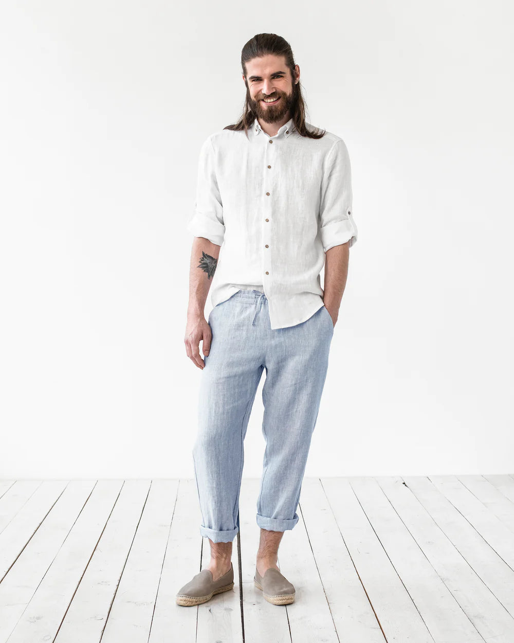 En manlig modell bär ett par blå linnebyxor och en vit linneskjorta.