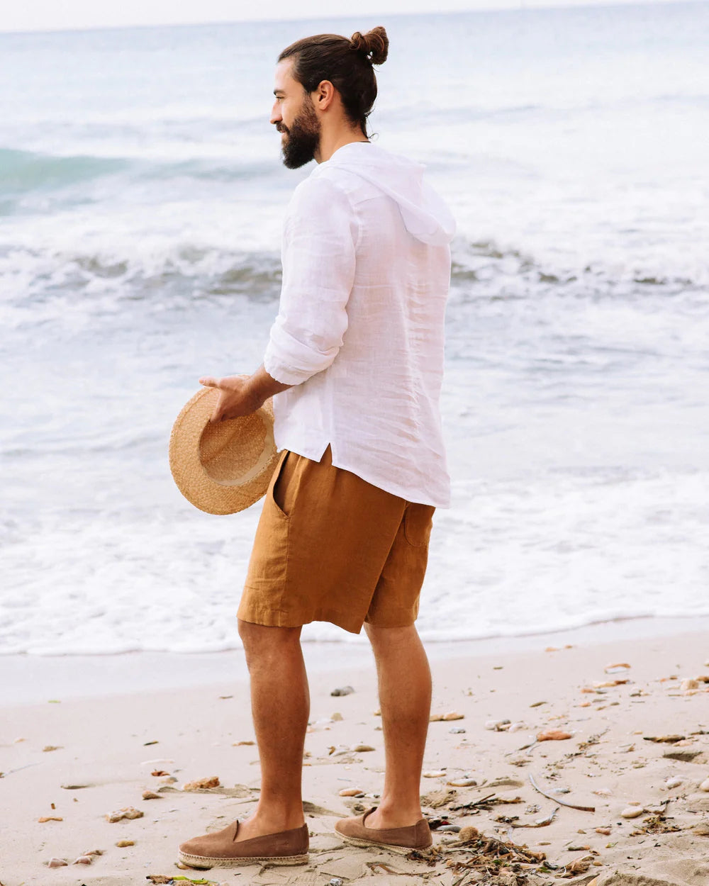 Mannen bär en vit linneskjorta och orange bruna linneshorts