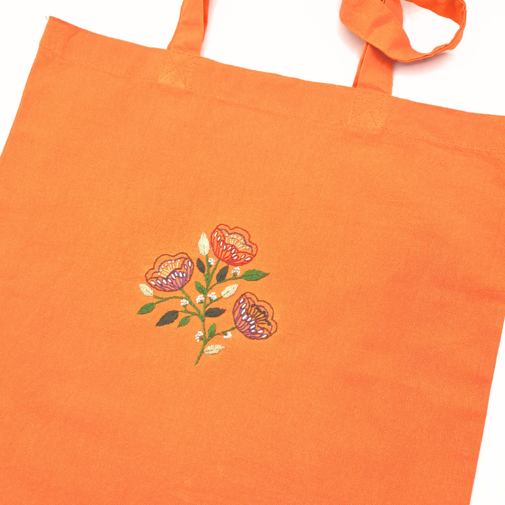 Ett blomsterbroderi på en orange tygväska 