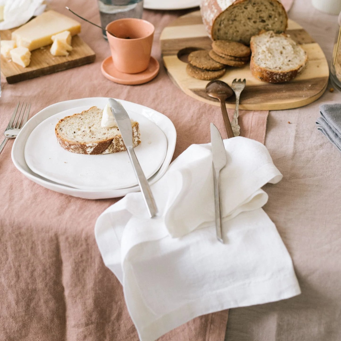 En frukostdukning med skivat bröd och textilier i vitt, beige och aprikos som ger ett varmt uttryck.
