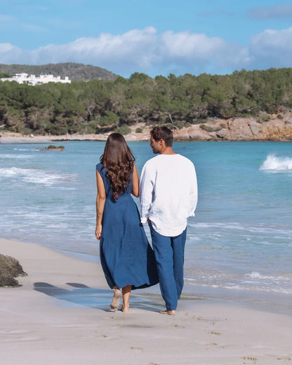 En dam och man går på en strand och har på sig blå linnekläder 