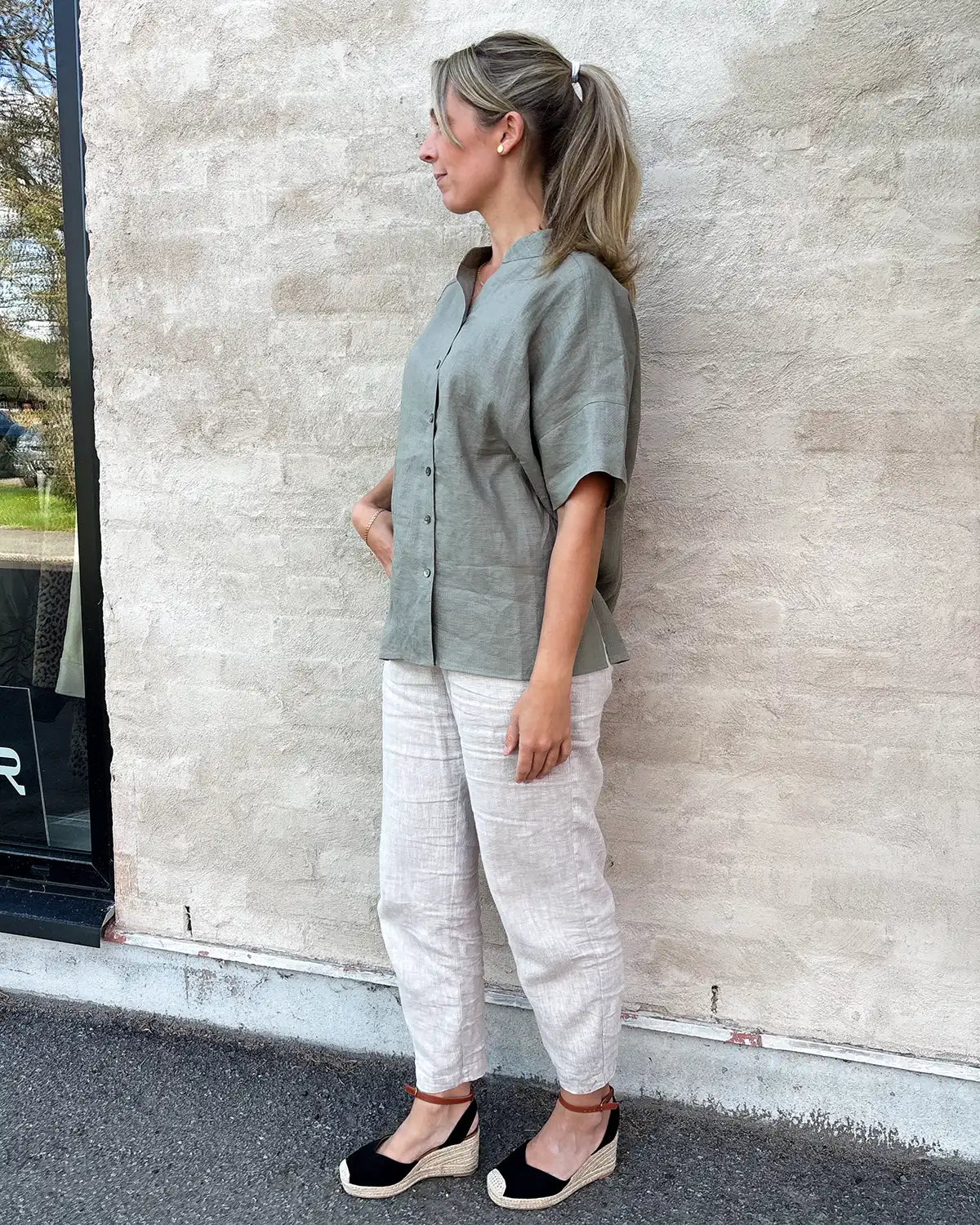 Modell bär kortärmad linneblus med murarkrage och beiga linnebyxor