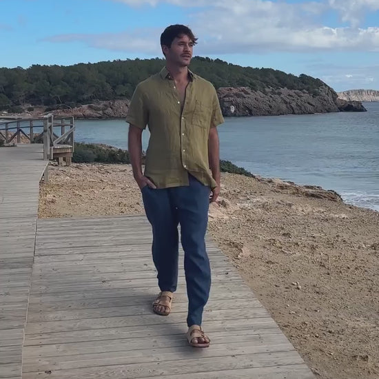 En film med en man som bär blå linnebyxor och en khakigrön skjorta 