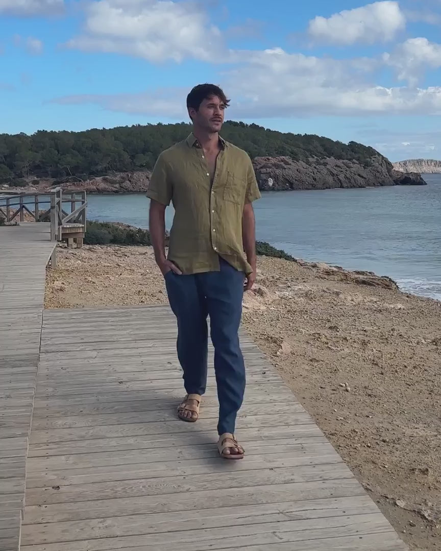En film med en man som bär blå linnebyxor och en khakigrön skjorta 