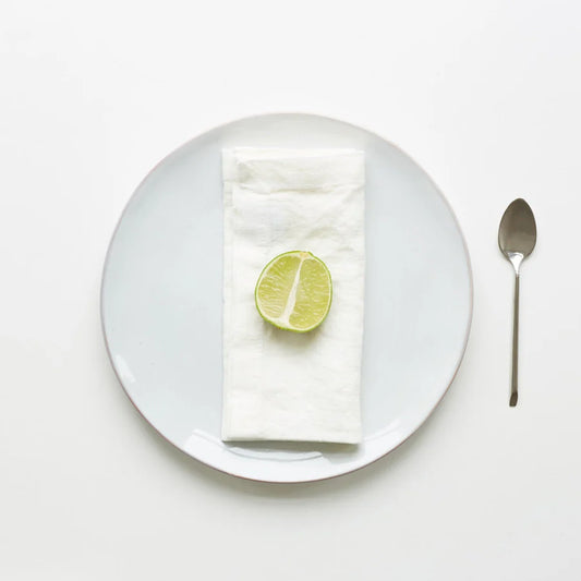 En vikt, vit tygservett på en vit tallrik med en halvt skivad lime på toppen.