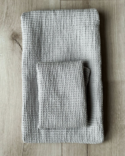Två grå våfflade linnehanddukar i olika storlekar ligger ihopvikta på varandra.