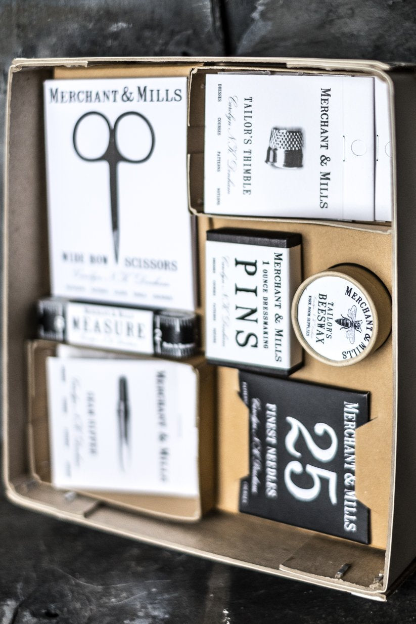 Ett stort sykit i pappers förpackning. Lådan innehåller sax, måttband, nålar och andra sybehör .
