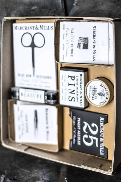 Ett stort sykit i pappers förpackning. Lådan innehåller sax, måttband, nålar och andra sybehör .