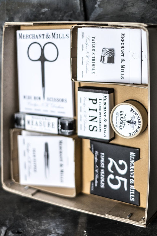 Ett stort sykit i pappers förpackning. Lådan innehåller sax, måttband, nålar och andra sybehör .