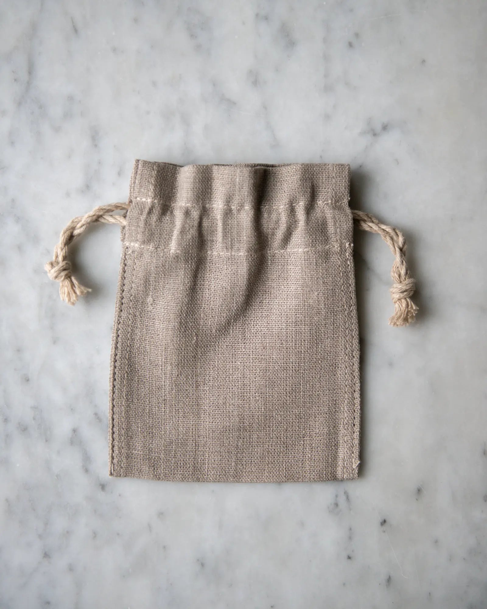 En liten handsydd linnepåse i beige ligger på en marmorskiva.