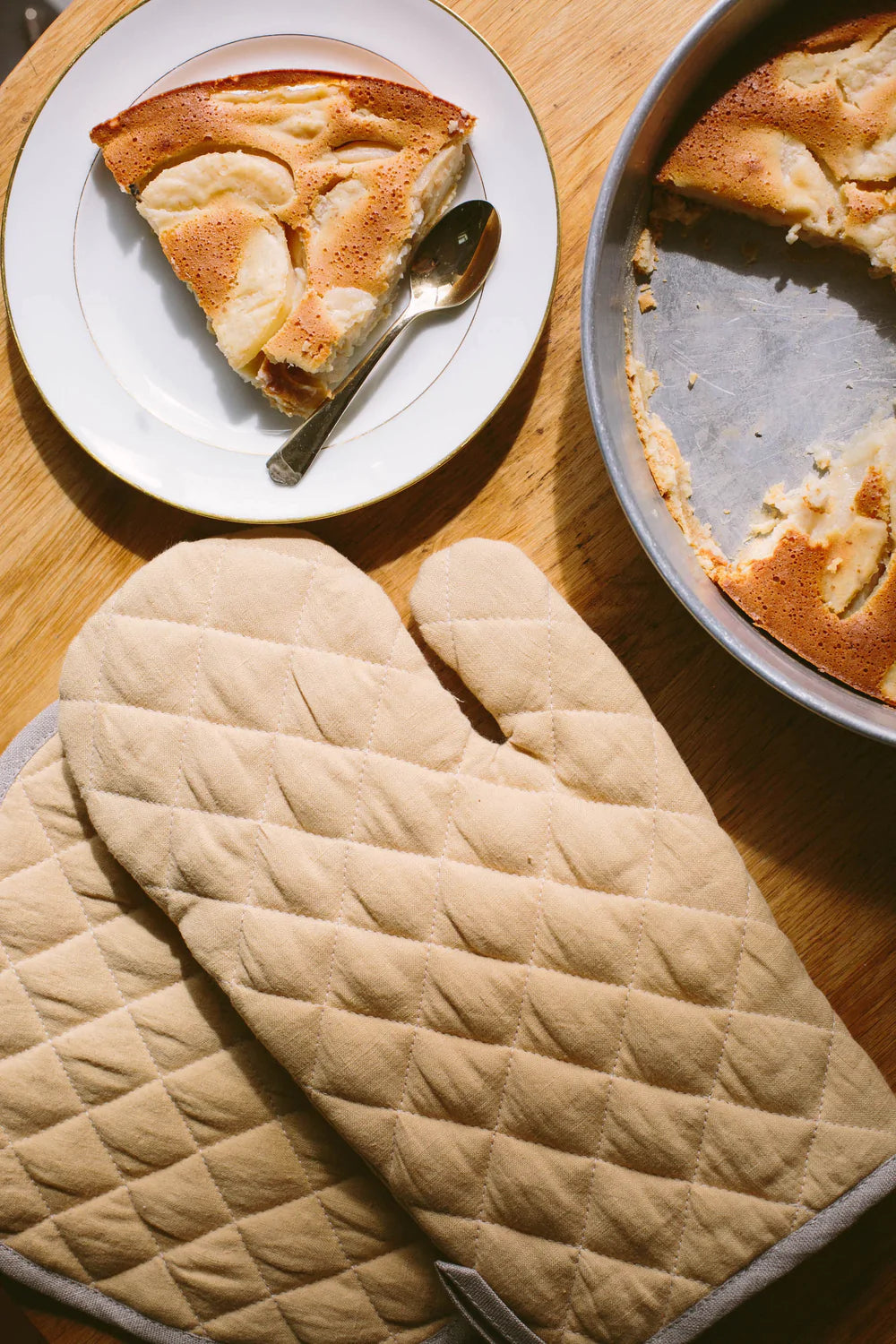 En beige quiltad grytvante och grytlapp ligger på ett bord.