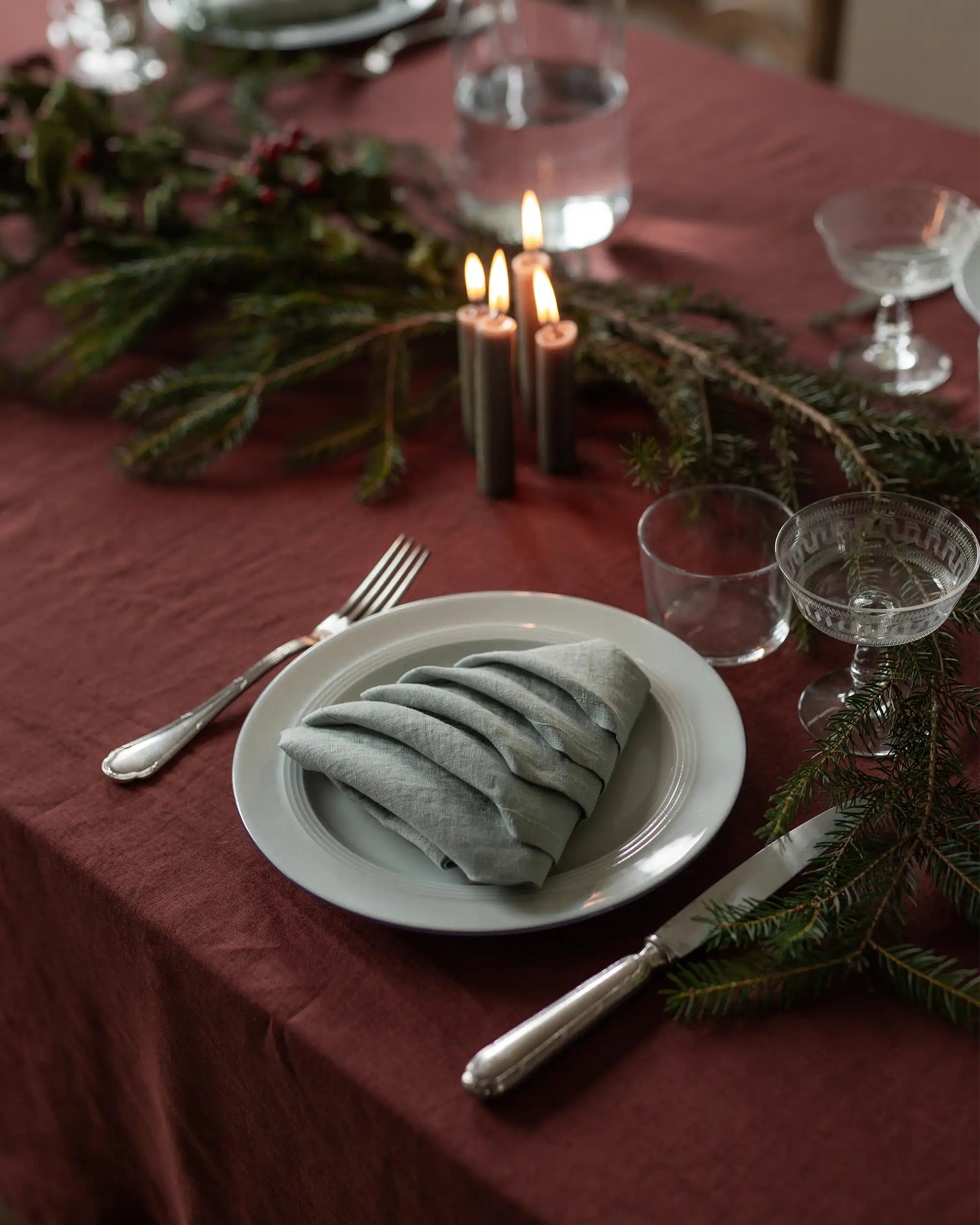 En ljusgrön linneservett som är vikt som en julgran ligger på en tallrik. 