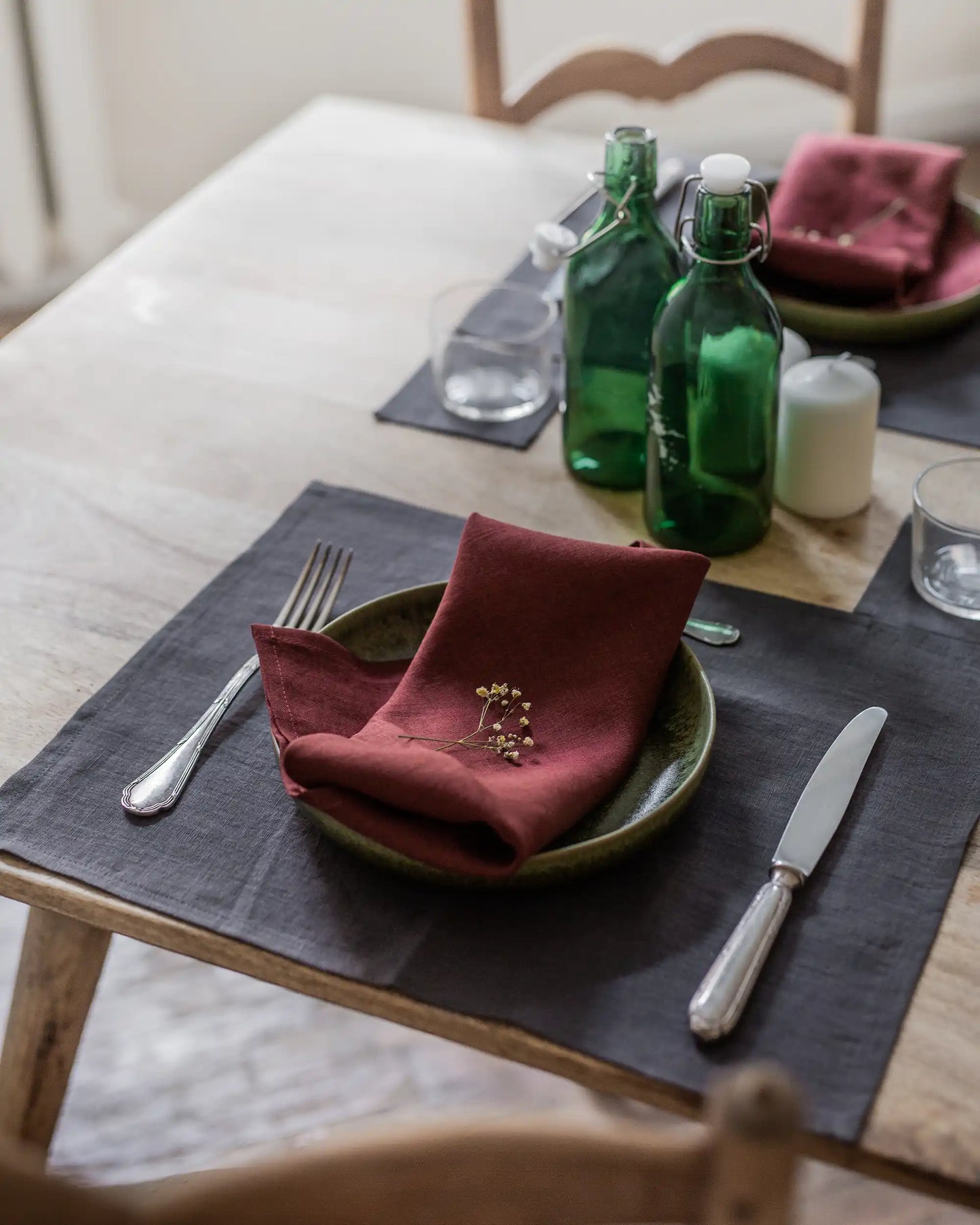 En röd tygservett i linne ligger ihopvikt på en tillrik till ett dukat bord. 