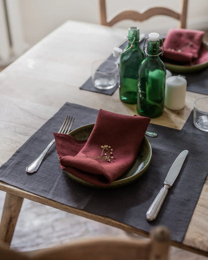 En röd tygservett i linne ligger ihopvikt på en tillrik till ett dukat bord. 