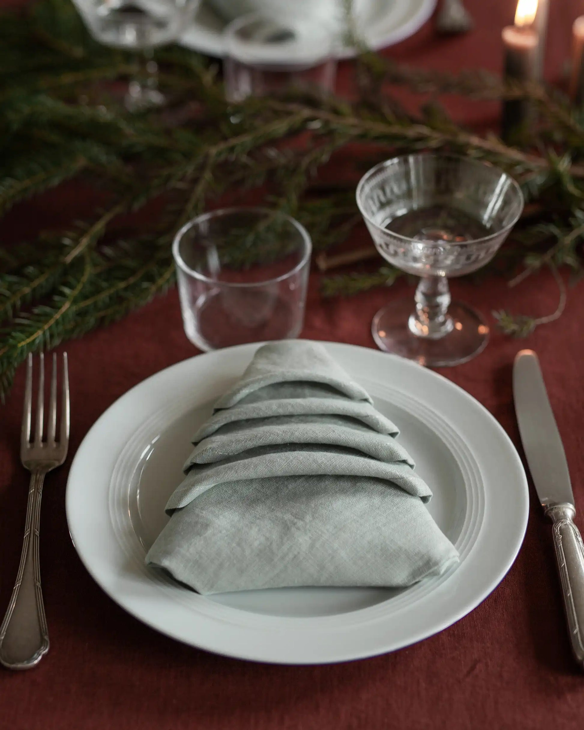En ljusgrön linneservett ligger vikt som en julgran på ett dukat bord. 