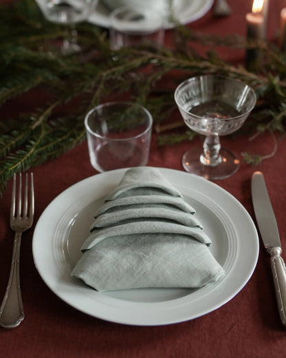 En ljusgrön linneservett ligger vikt som en julgran på ett dukat bord. 