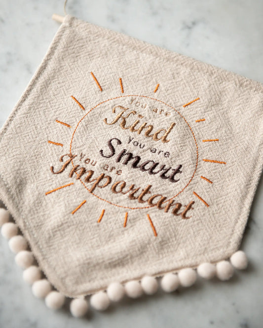 En beige linnevimpel med en broderad text.